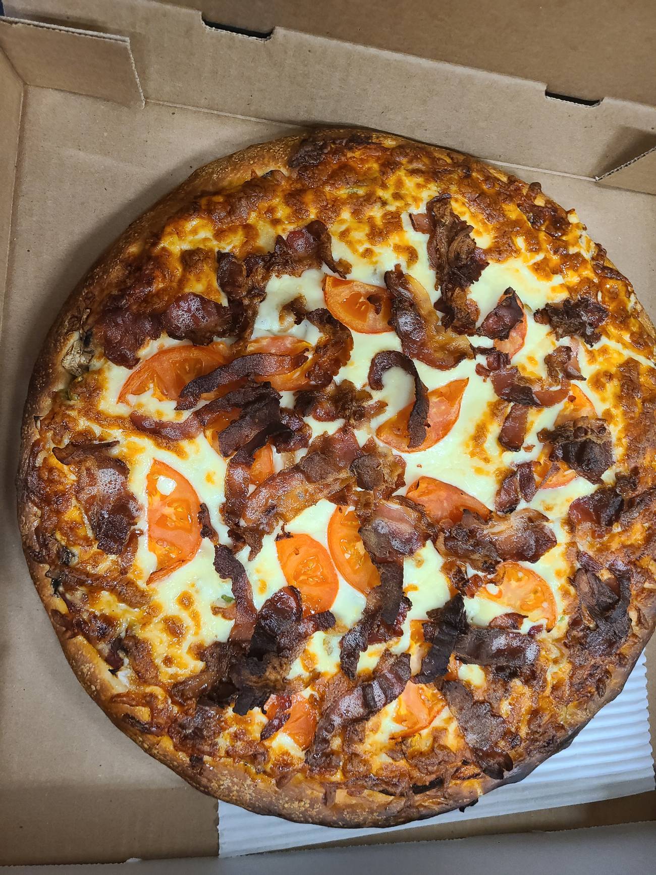 Bronson's Special pizza in an open box, topped edge to edge with bacon, tomato and melted cheese.
