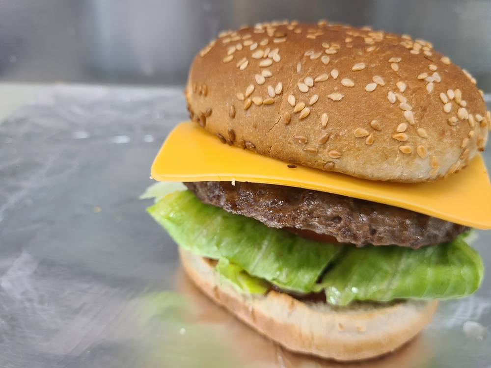 Cheeseburger on a sesame bun with lettuce and a slice of cheese, made at the counter.