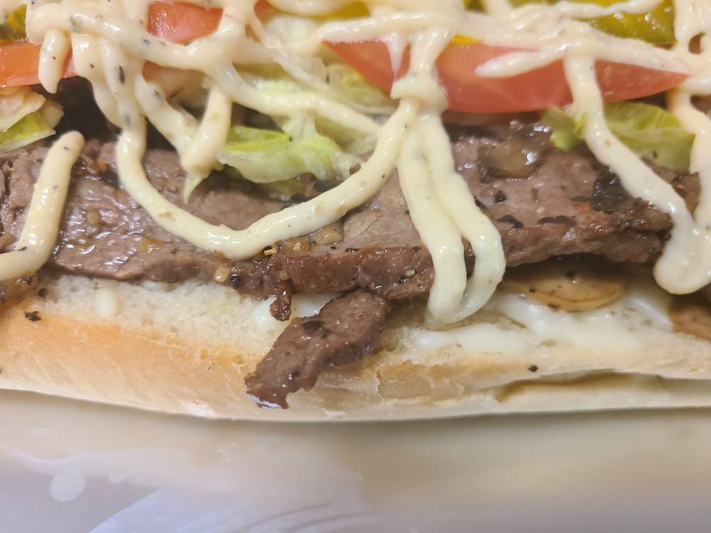 Steak sub on a soft roll, layered with sliced steak, lettuce, tomato and sauce.