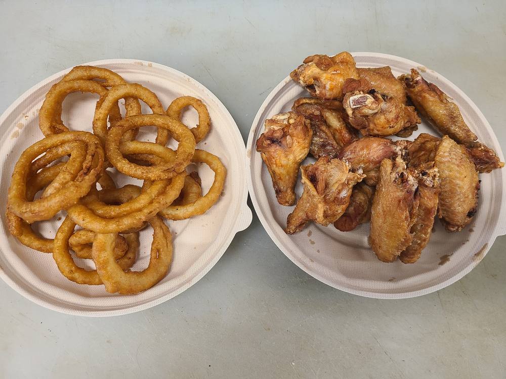 A plate of golden onion rings beside a plate of fried chicken wings.